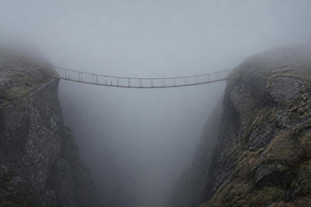 A frayed rope bridge crossing a fog-filled chasm between two cliffs