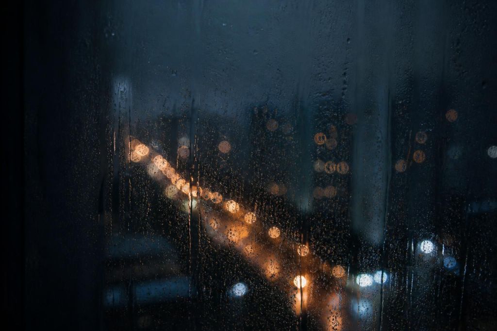 A rain-streaked window at night with city lights blurred beyond the glass